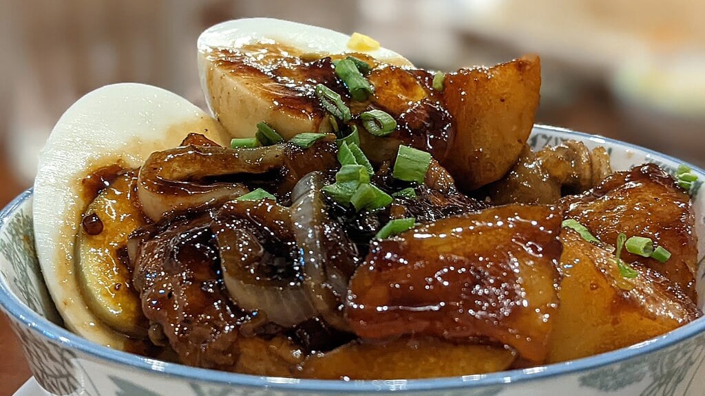 A plate of chicken adobo with tender chicken pieces and golden-brown potatoes, simmered in a savory sauce of soy sauce, vinegar, garlic, and spices