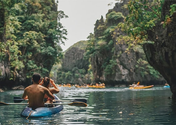 Tourists kayaking in the Small Lagoon, El Nido, Palawan, surrounded by towering limestone cliffs and lush greenery, with turquoise-green waters shimmering under the sun