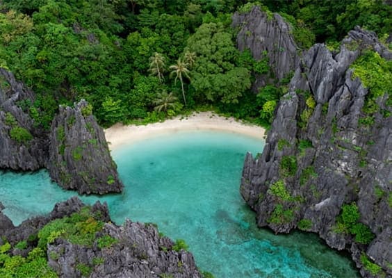 Aerial view of Palawan’s Secret Beach, highlighting dramatic limestone cliffs rising from clear turquoise water along the island’s secluded coastline.