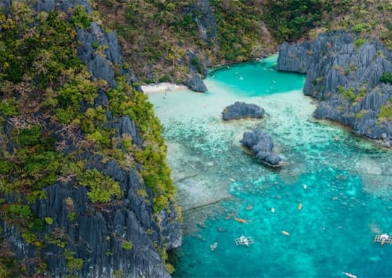 Aerial view of Secret Beach in Palawan, Philippines, showing turquoise waters, white sandy shores, and lush green cliffs surrounding the cove.