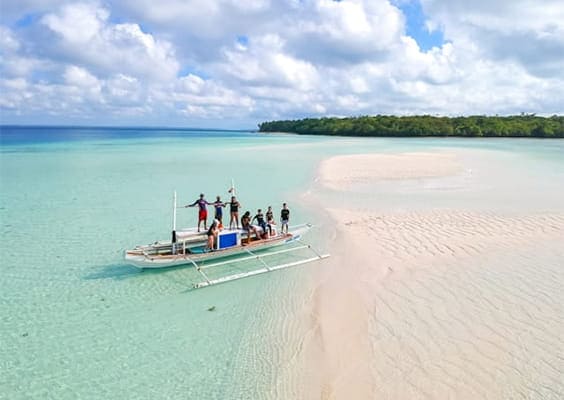Boat with travelers navigating shallow turquoise waters around a pristine white sand island in Balabac