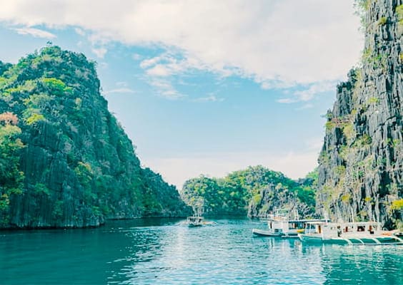 Tourist boats floating among rugged limestone cliffs in Coron